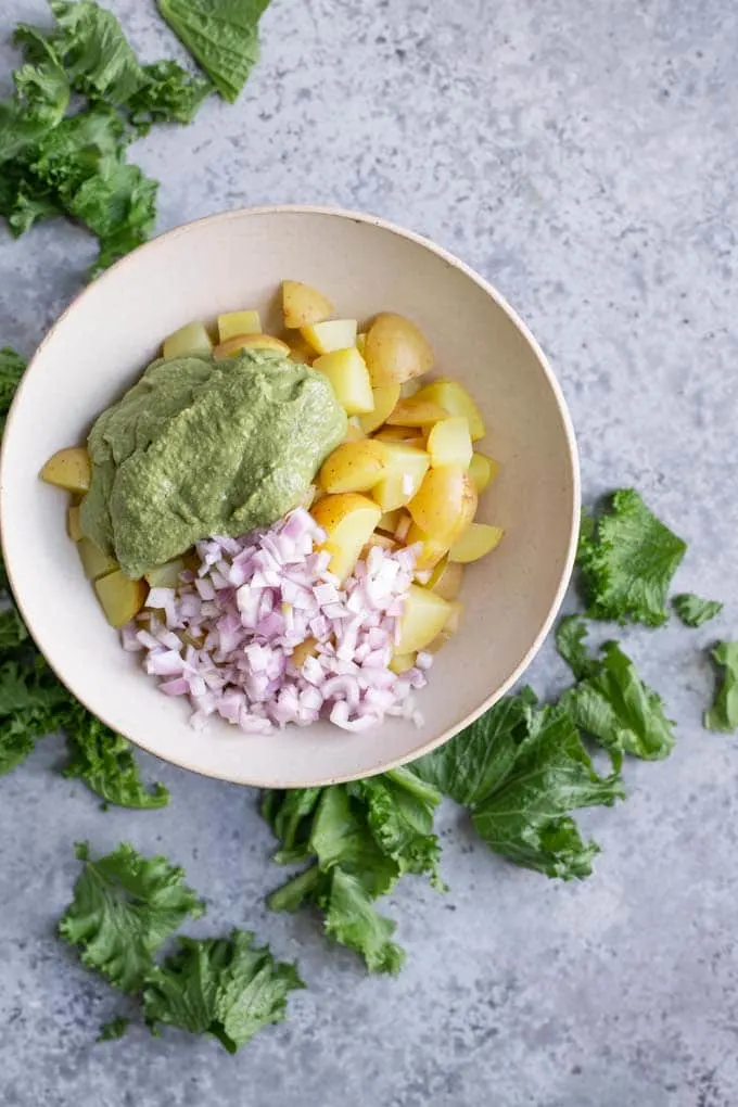 potatoes, pesto, and onion combined in bowl before mixing