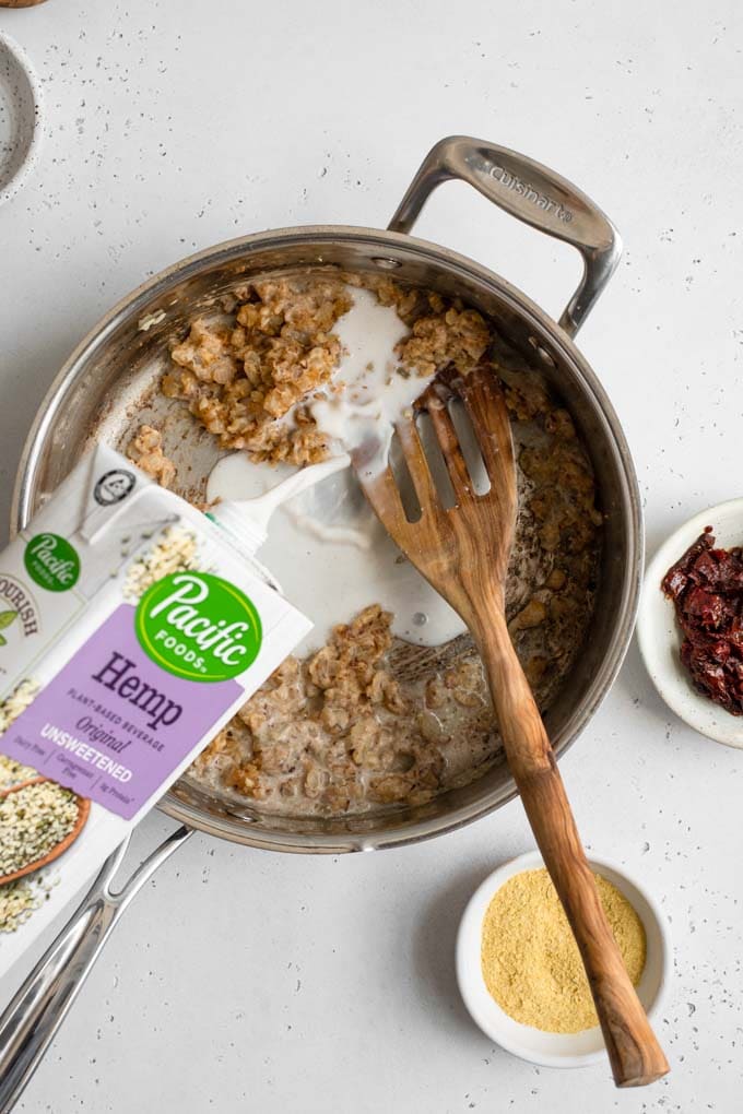 pouring unsweetened hemp milk into pot over cooked flour and onions