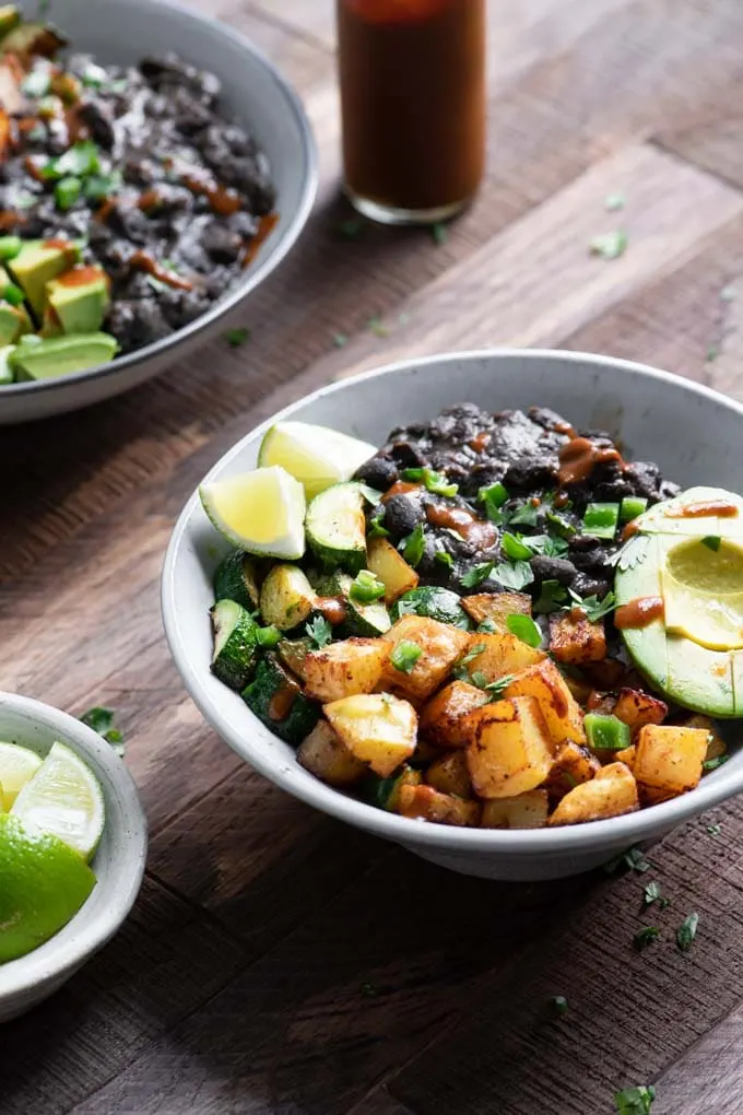 rice bowl with seasoned black beans, ancho roasted potatoes, zucchini, lime wedges, and rice