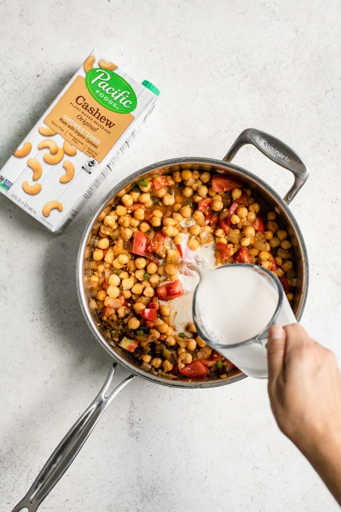 pouring cashew milk into chickpea and tomato curry