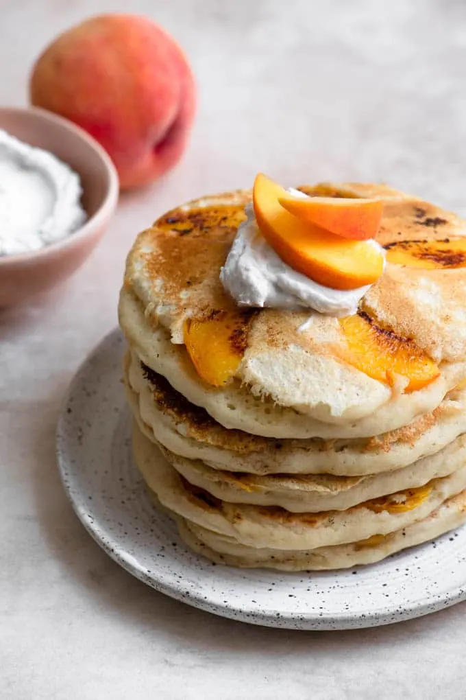 stack of vegan peach pancakes with a dollop of vegan whipped cream and a couple slices of peaches on top