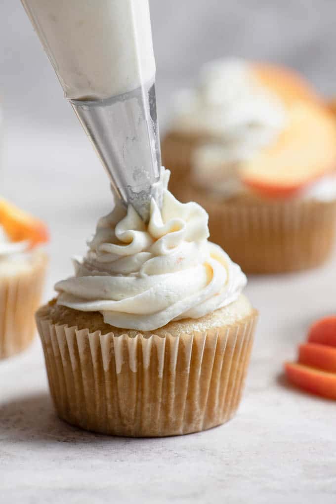 piping peach frosting onto cupcake