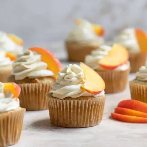 peach cupcakes frosted with a peach slice resting on frosting