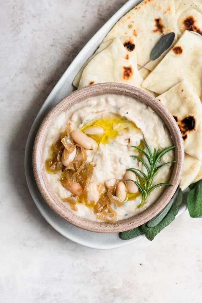 caramelized onion white bean dip garnished with rosemary sprig and drizzle of olive oil