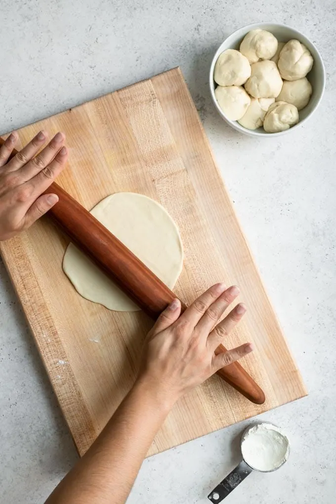 rolling out a flatbread on a wood cutting board with a rolling pin
