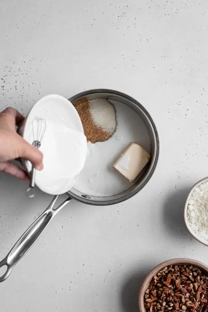 pouring cornstarch slurry into small pot where ingredients are combined for coconut pecan frosting