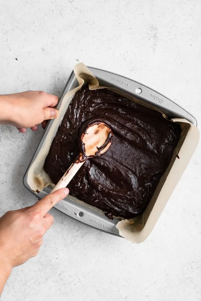 spreading brownie batter in pan with wooden spoon