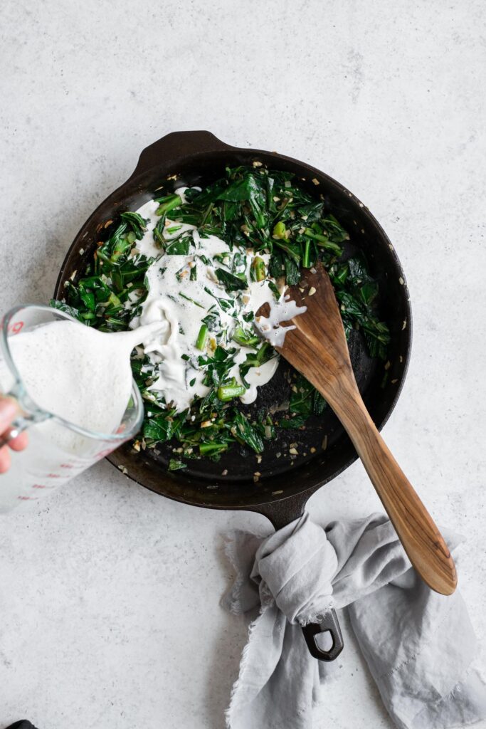 pouring cashew cream into sautéed collard greens