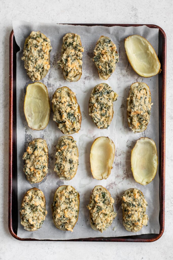 baked potato skins being filled with cheesy creamed collard green potato filling
