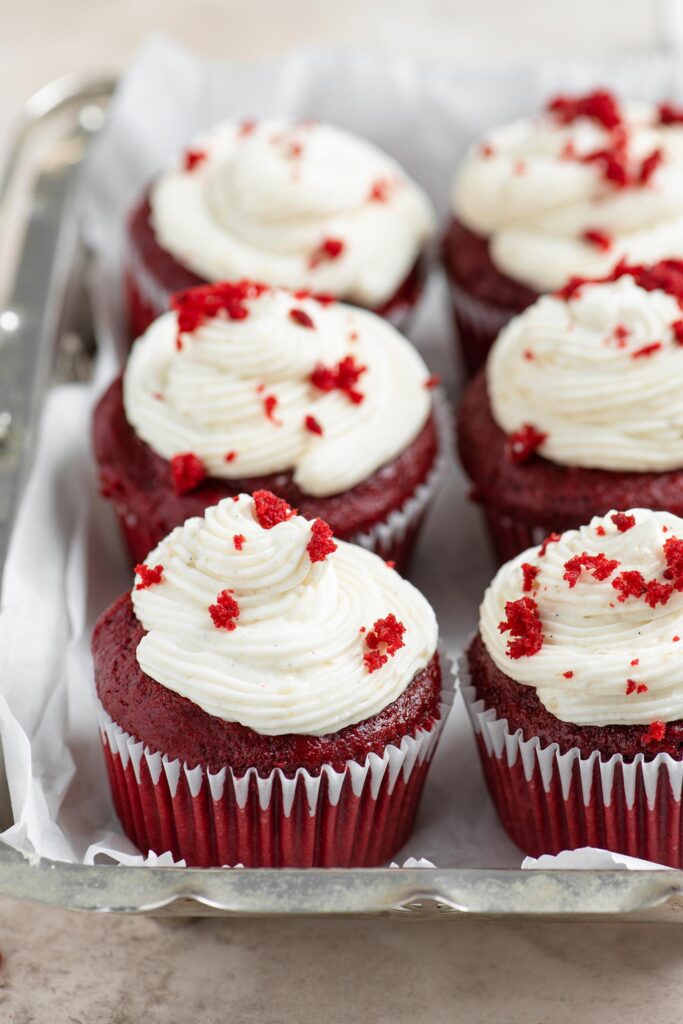 six frosted vegan red velvet cupcakes in a metal serving dish