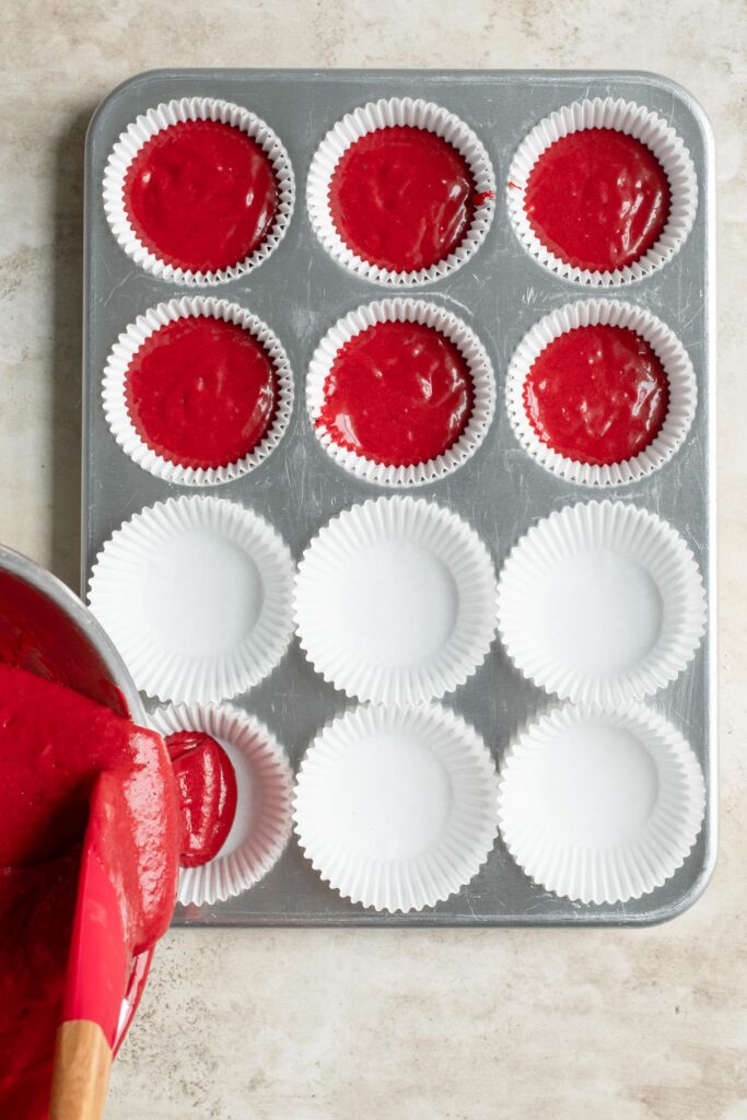 pouring cake batter into tin prepared with cupcake liners, 6 cups are already filled