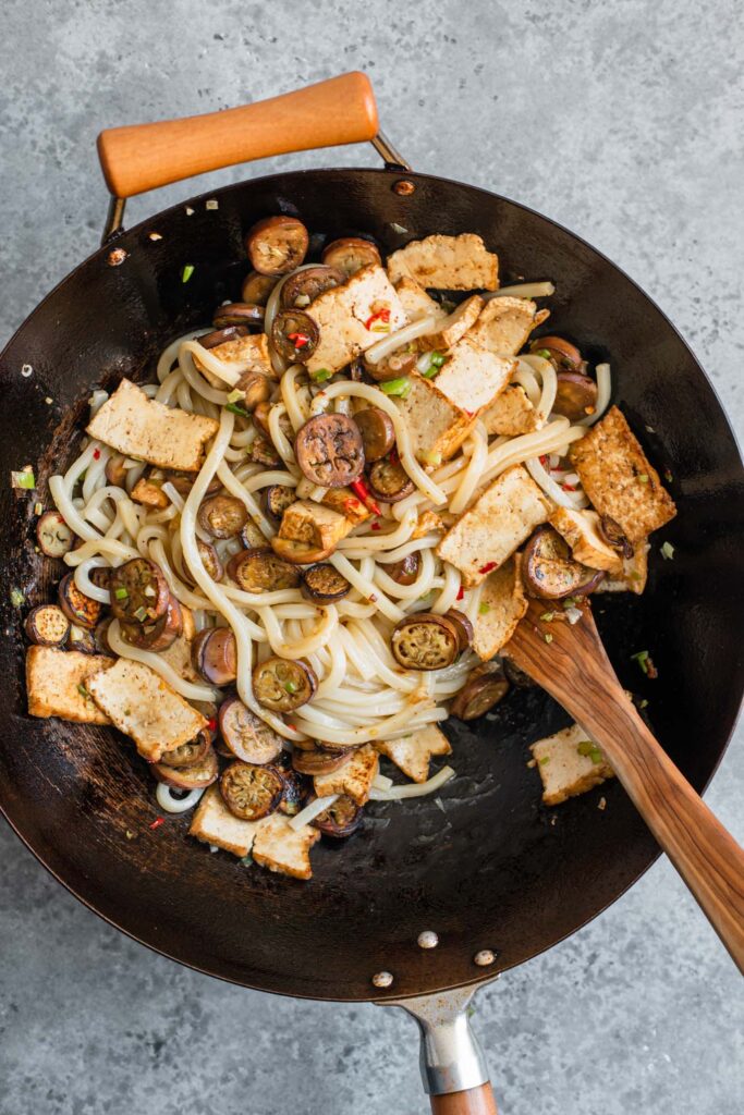 spicy sichuan noodles with tofu and eggplant tossed together in a wok