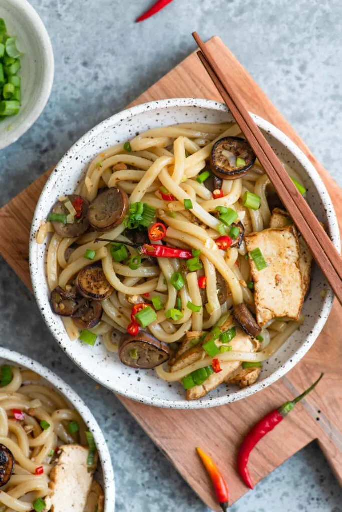 overhead shot of sichuan noodles with eggplant garnished with Thai chilies and green onions