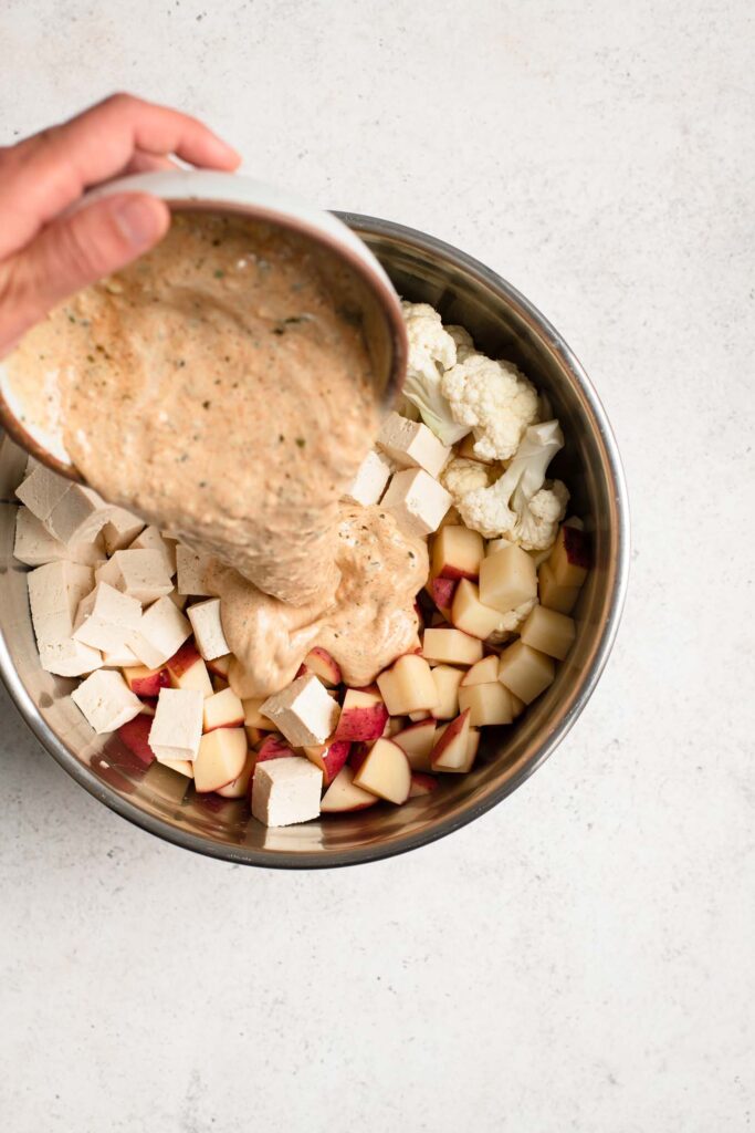 pouring tandoori yogurt sauce over cut tofu, potato, and cauliflower