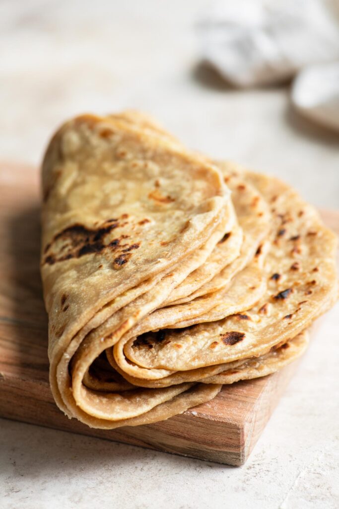 eight homemade roti folded in half in the center sitting on cutting board