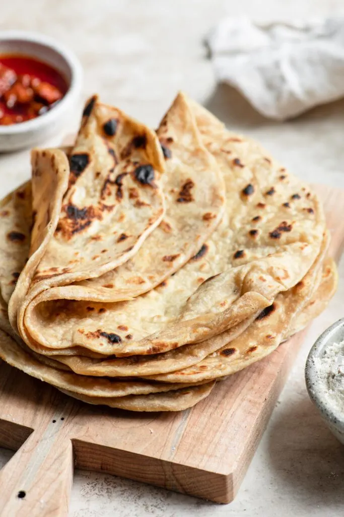 roti on a cutting board with a small bowl of aachar in the background