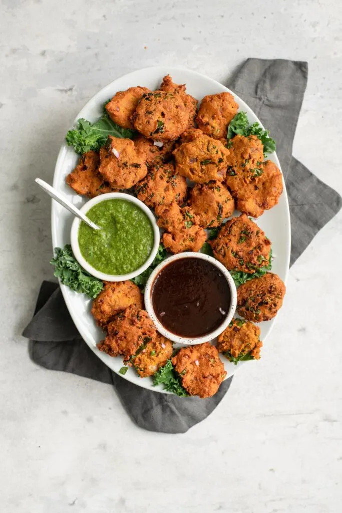 kale pakoras served with tamarind chutney and cilantro chutney on a plate