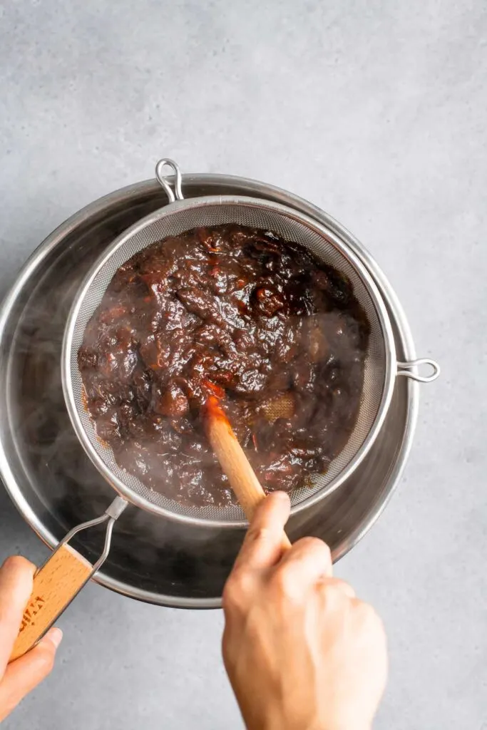 pushing tamarind juice through a metal sieve to remove the seeds and fibrous pulp