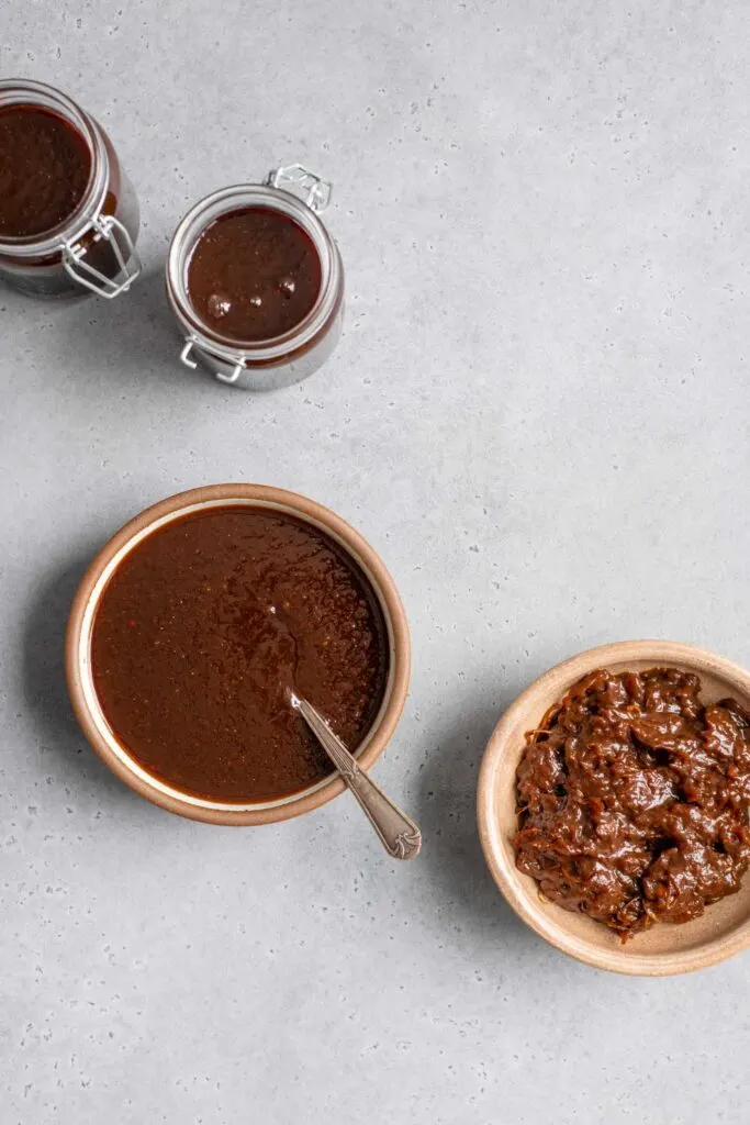 two jars and a bowl filled with tamarind chutney, with a second bowl showing the separated pulp