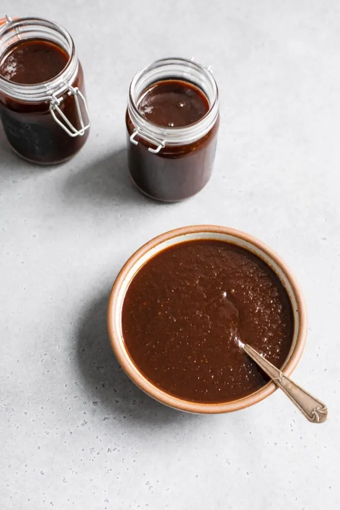 tamarind chutney served in a bowl with two jars filled behind it