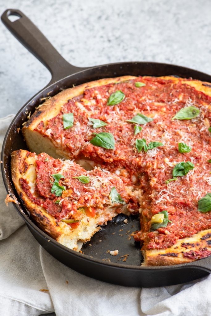 Deep dish pizza with one slice removed and a second cut in the pan