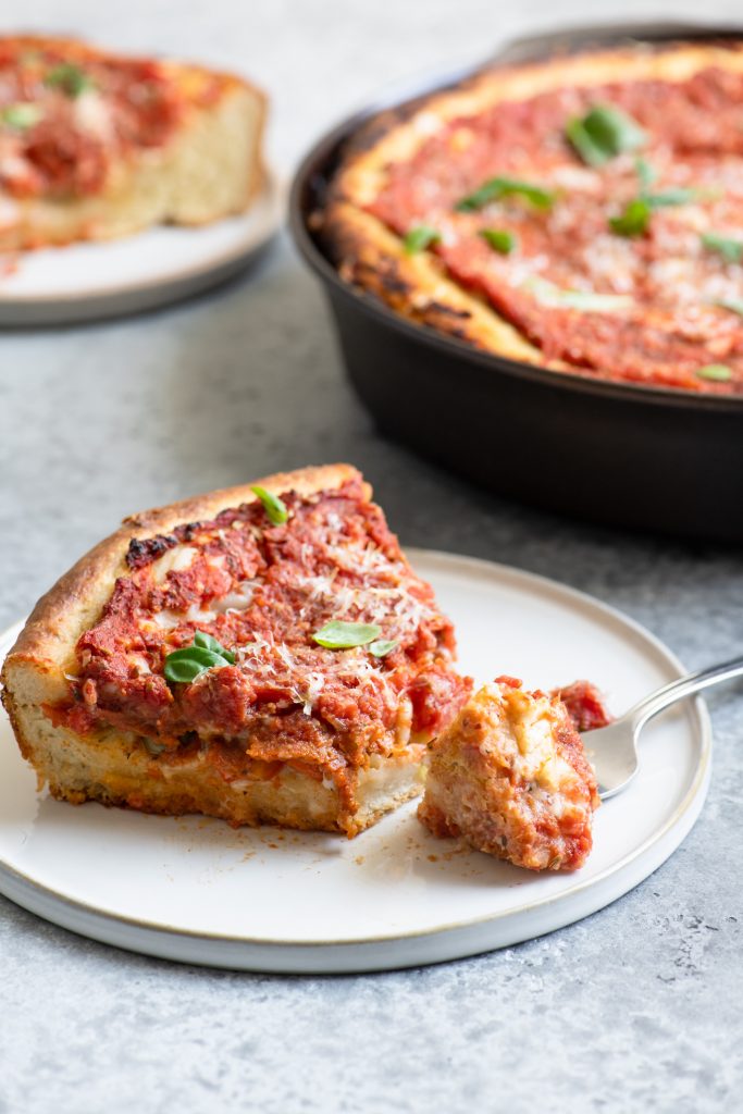 slice of pizza with one bite on a fork and the whole pizza and a second slice in the background