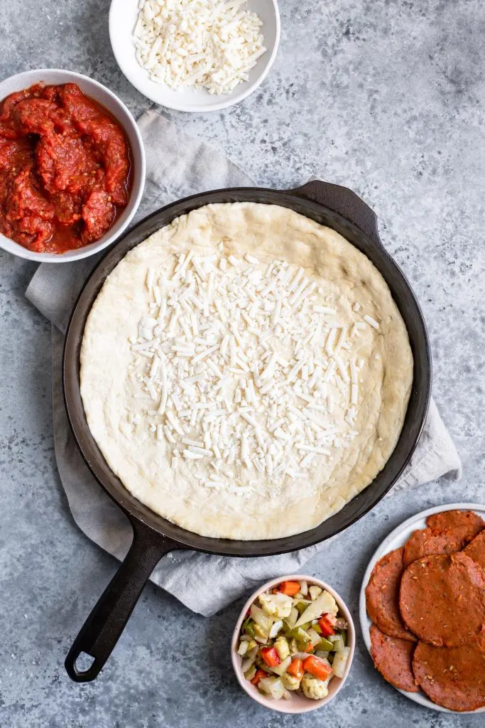 assembling deep dish pizza: sprinkling of cheese in bottom of dough