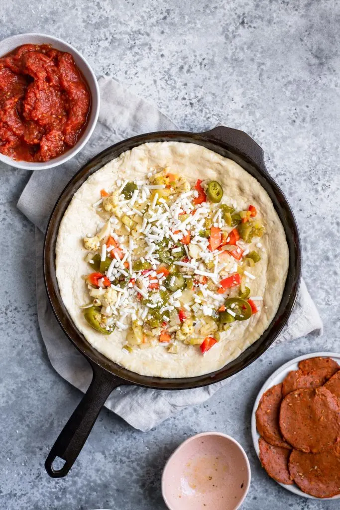 assembling deep dish pizza: light sprinkling of mozzarella over vegetables