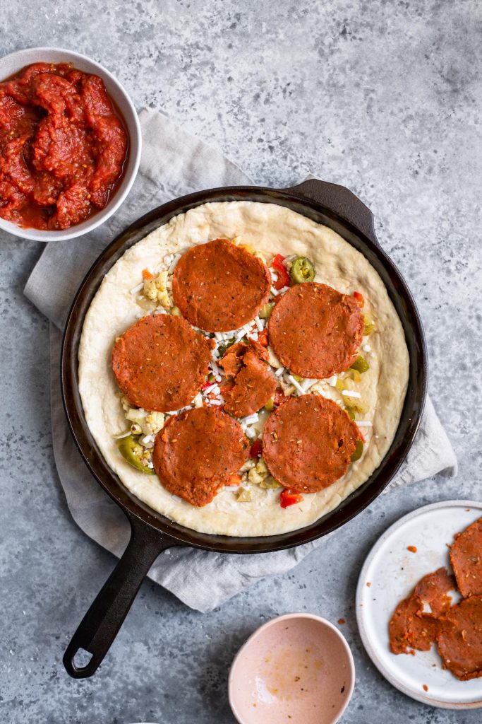 assembling deep dish pizza: vegan pepperoni added over vegetables