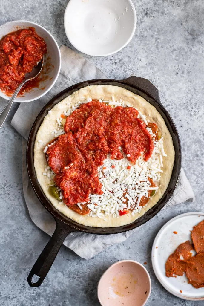 assembling deep dish pizza: spreading the thick tomato sauce over the cheese