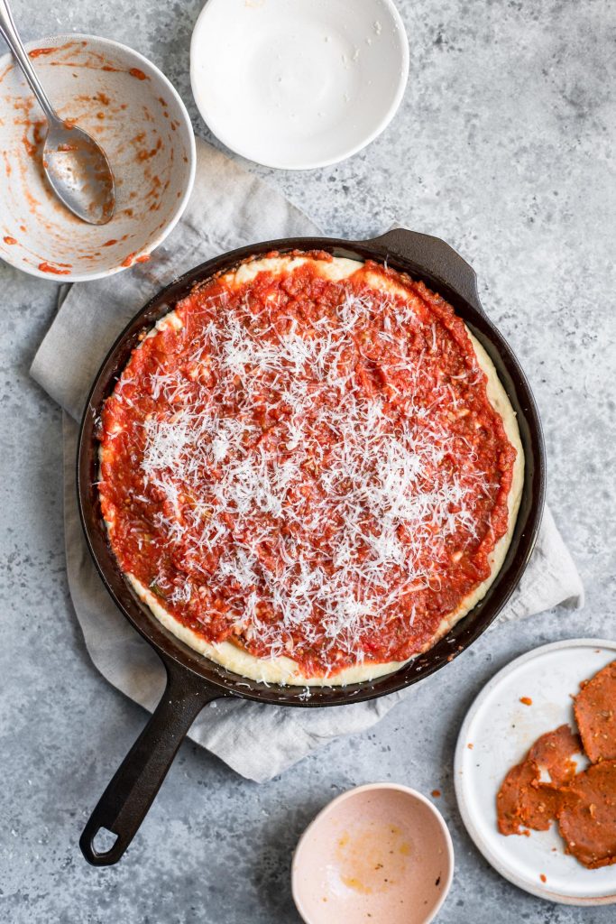 Maak een diepe pizza klaar voor het bakken met de Parmezaanse kaas bovenop de saus