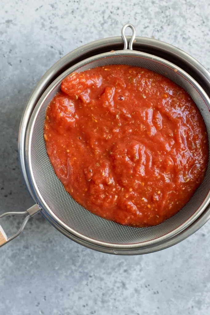 draining tomato sauce in a fine mesh strainer over a mixing bowl