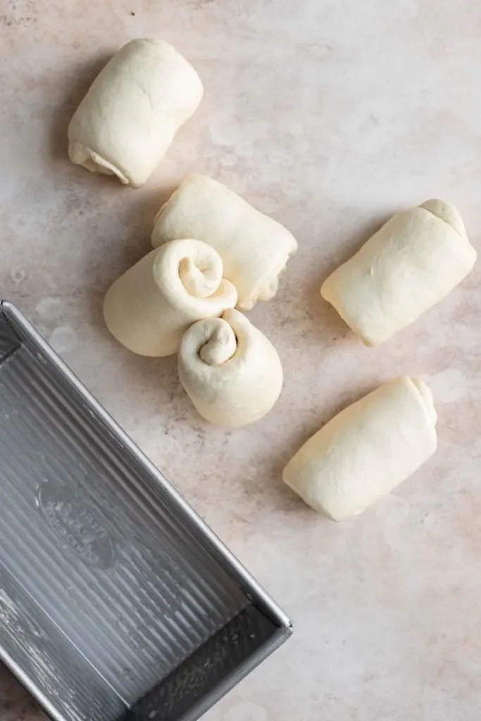 6 segments of rolled dough next to greased loaf pan