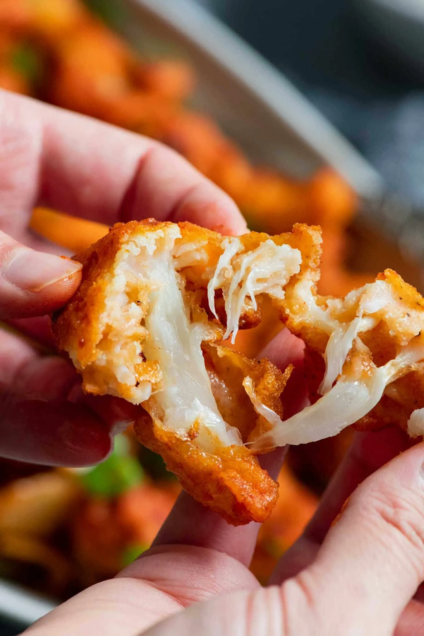 a piece of cauliflower being torn in half to show the battered crust and cooked cauliflower inside