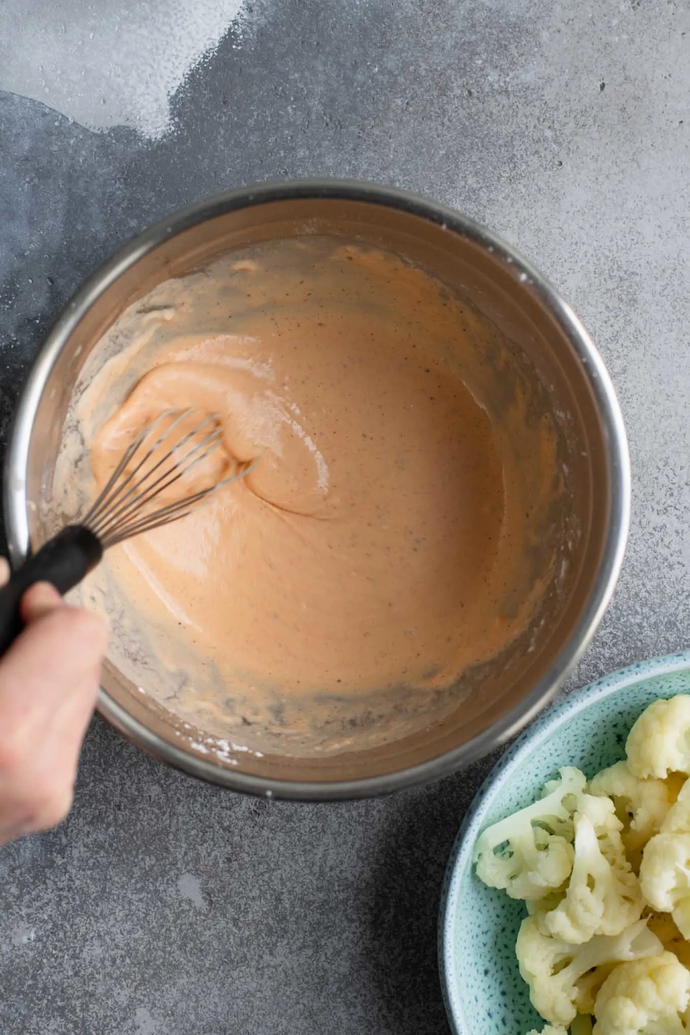 gobi batter in a mixing bowl with steamed cauliflower in a second bowl