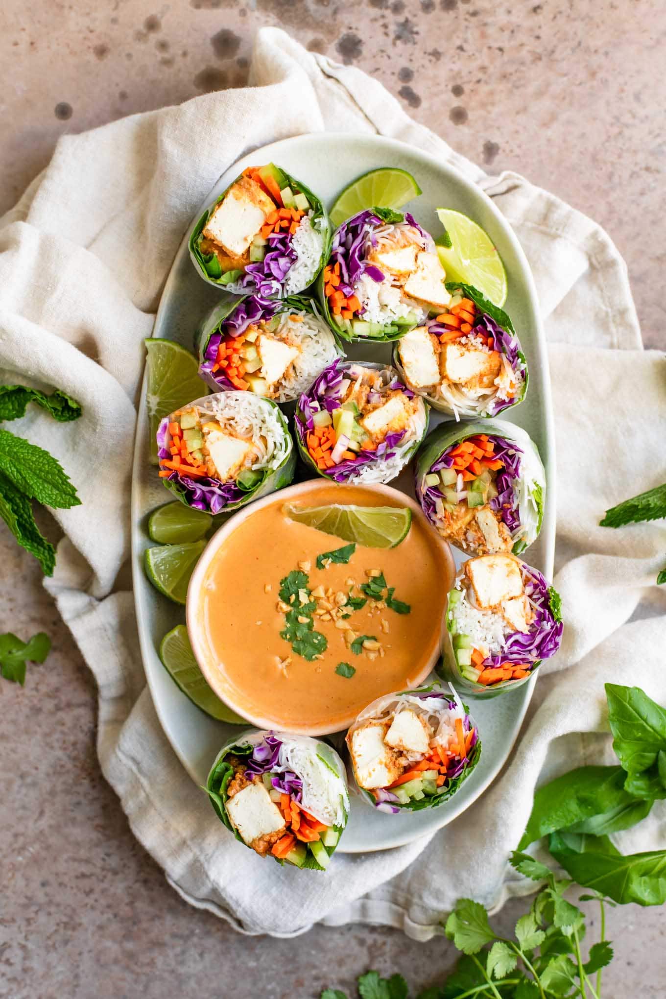 peanut tofu spring rolls cut in half and placed on a platter with lime wedges and a bowl of peanut sauce for dipping