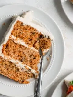 slice of vegan carrot cake on a plate with a fork taking a piece out of the corner