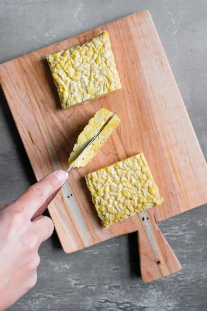 a knife slicing into the middle third of the cut tempeh