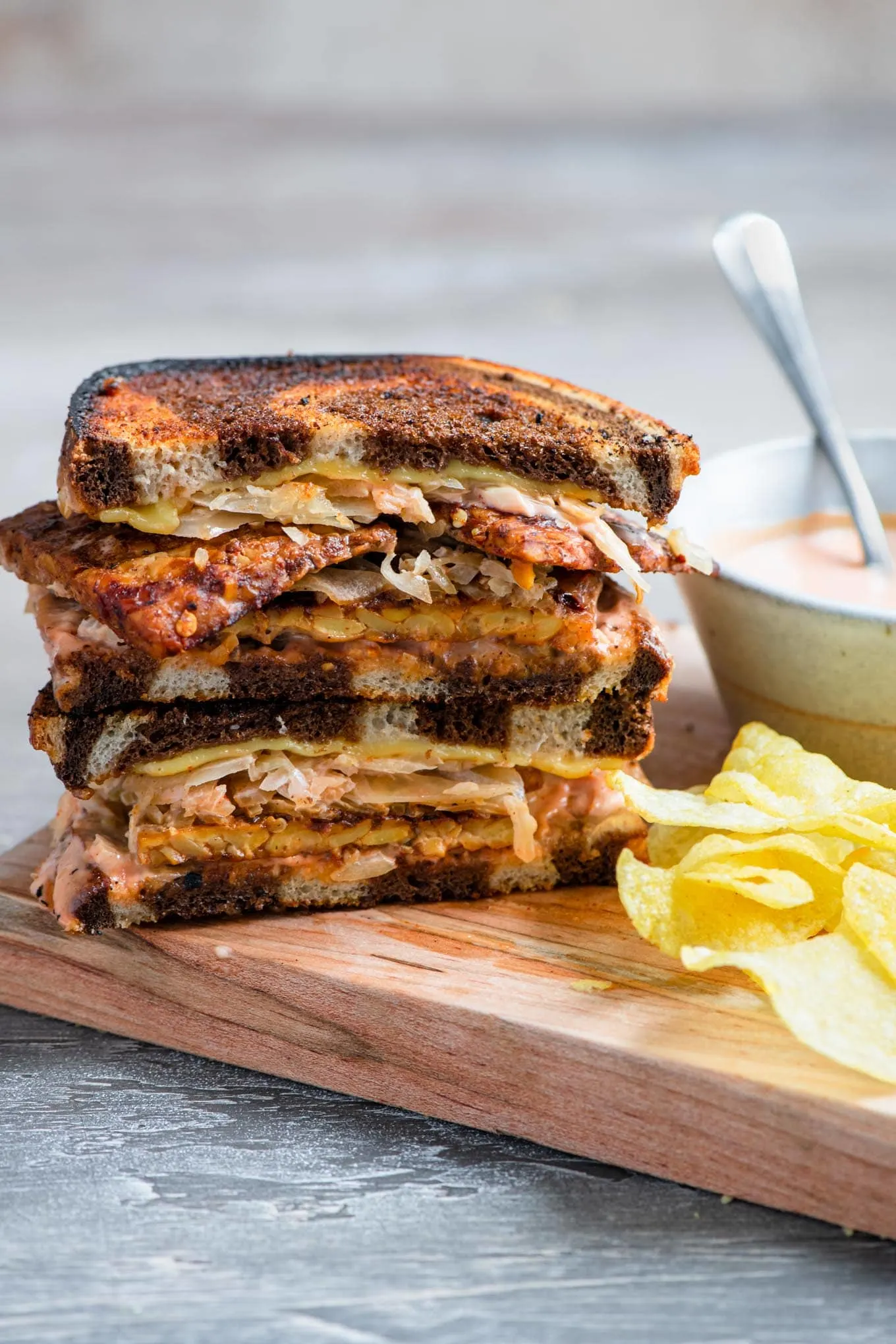 vegan reuben sandwich on a cutting board with extra thousand island dressing on the side and potato chips