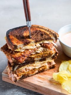 a vegan reuben sandwich cut in half and stacked with a steak knife piercing into the sandwiches