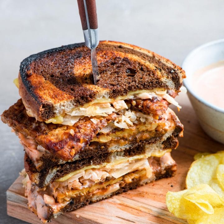 a vegan reuben sandwich cut in half and stacked with a steak knife piercing into the sandwiches