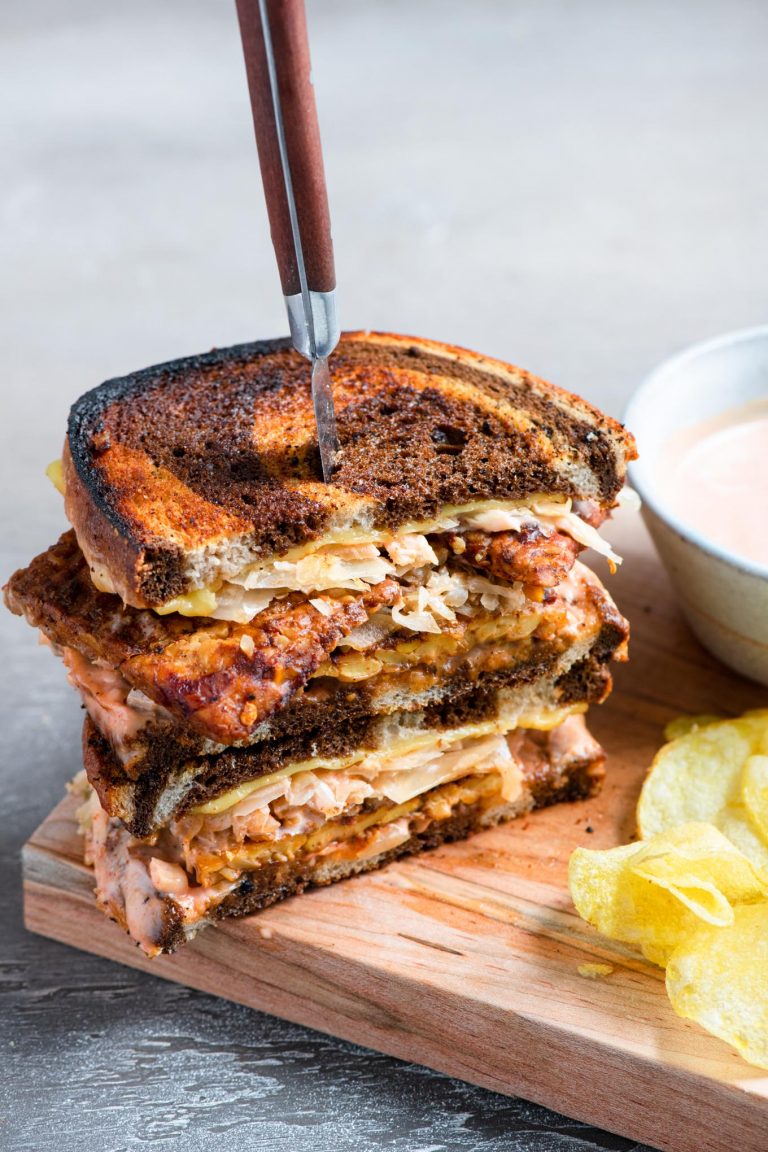 a vegan reuben sandwich cut in half and stacked with a steak knife piercing into the sandwiches
