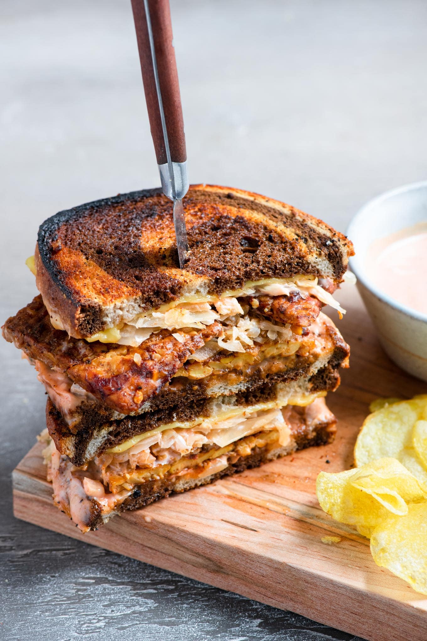 a vegan reuben sandwich cut in half and stacked with a steak knife piercing into the sandwiches