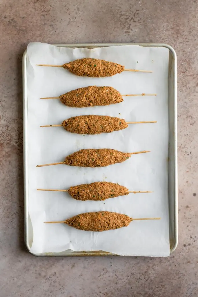 sheekh kababs formed and skewered on a parchment lined baking tray