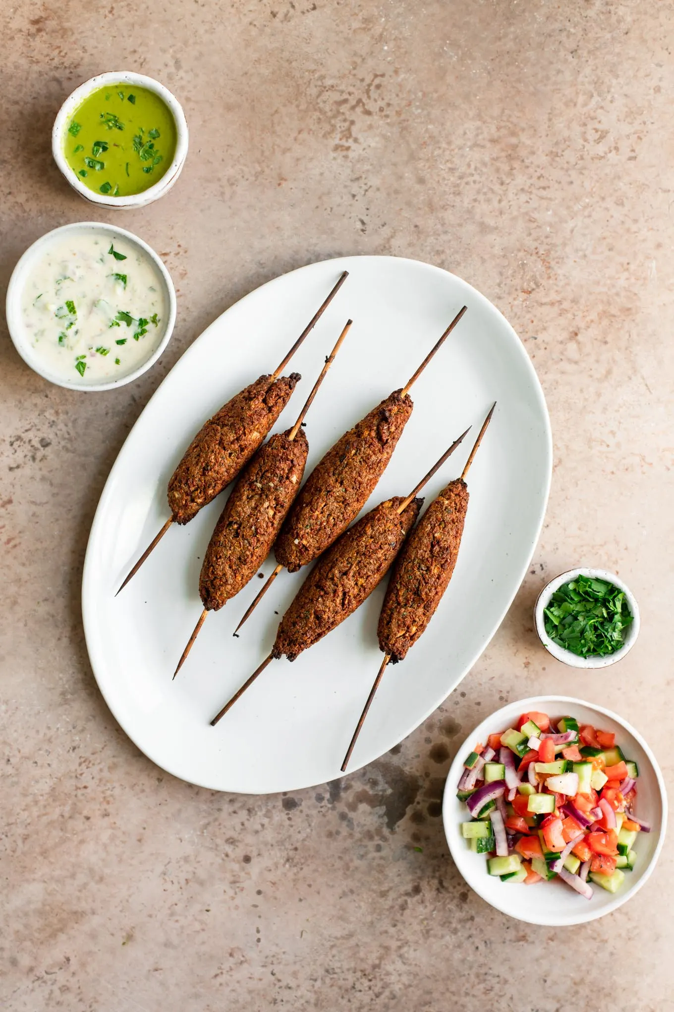 baked vegan sheekh kababs on a plate with sides of chutney, raita, and salad