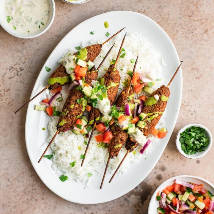 vegan sheekh kababs on a platter of basmati rice, topped with raita, cilantro chutney, katchumber salad, and cilantro