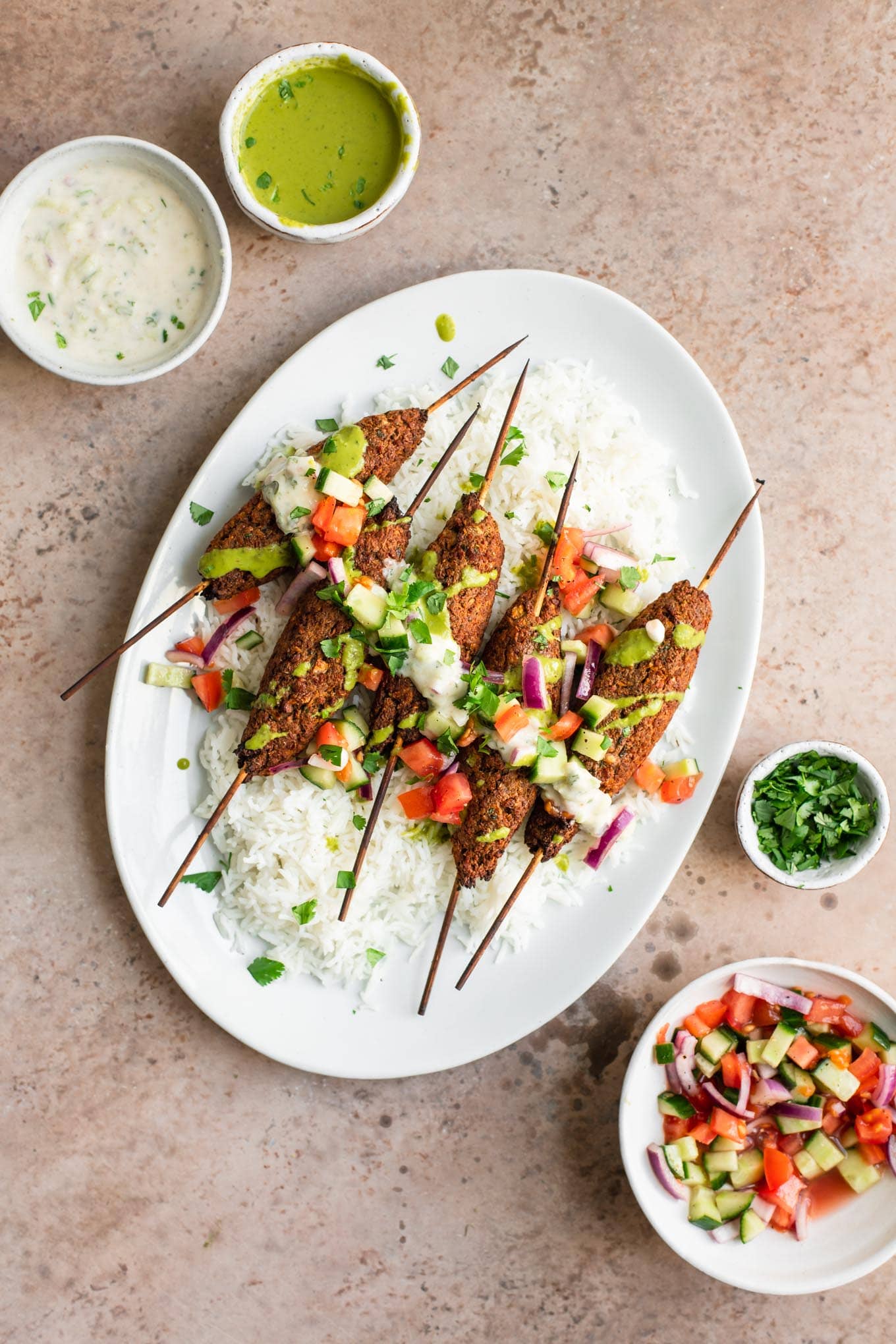 vegan sheekh kababs on a platter of basmati rice, topped with raita, cilantro chutney, katchumber salad, and cilantro