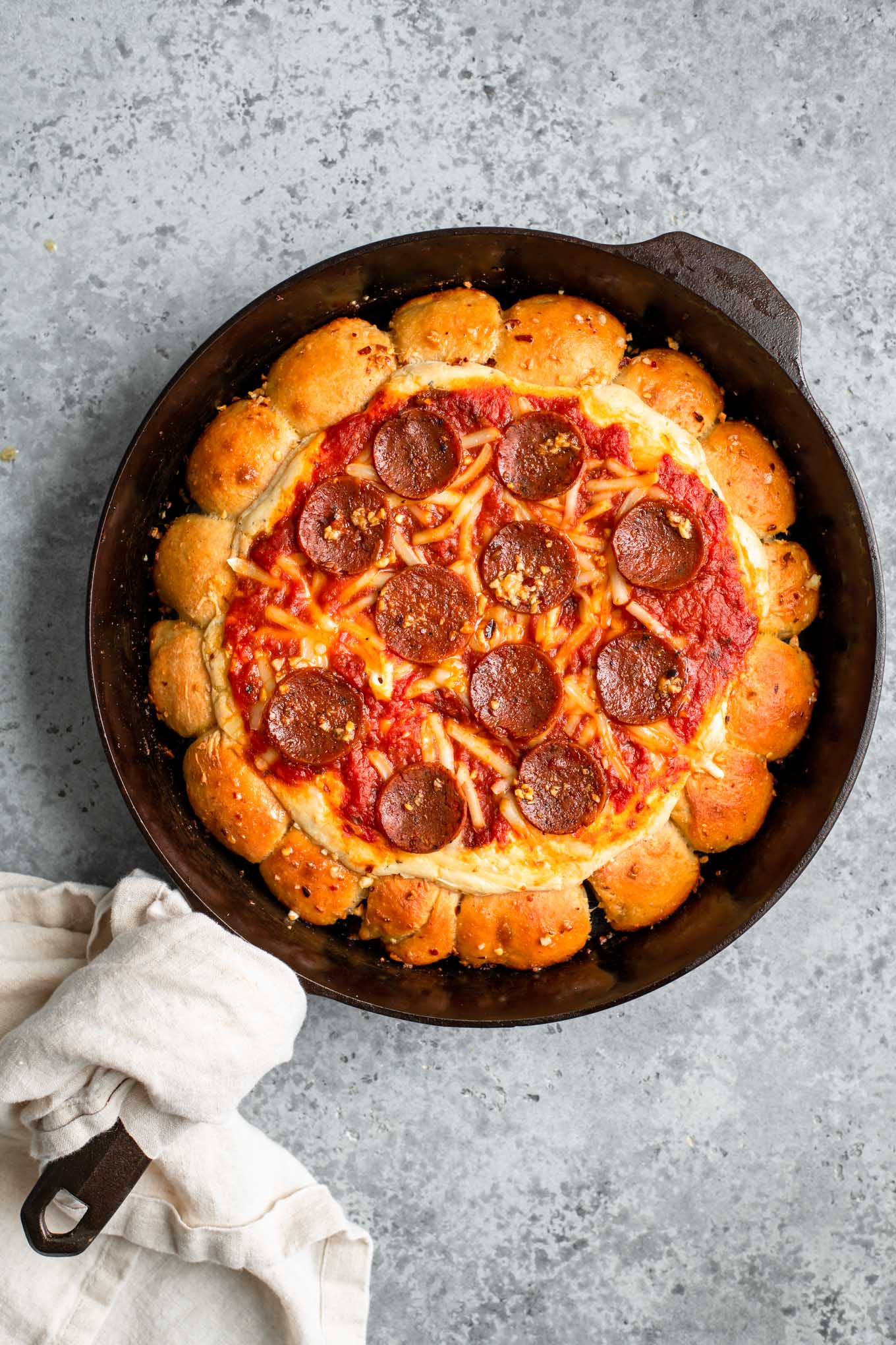 vegan skillet pizza dip served in cast iron skillet with tan linen wrapped around handle