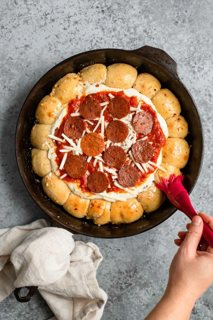 vegan pepperoni topped dip and brushing garlic butter over edges of rolls