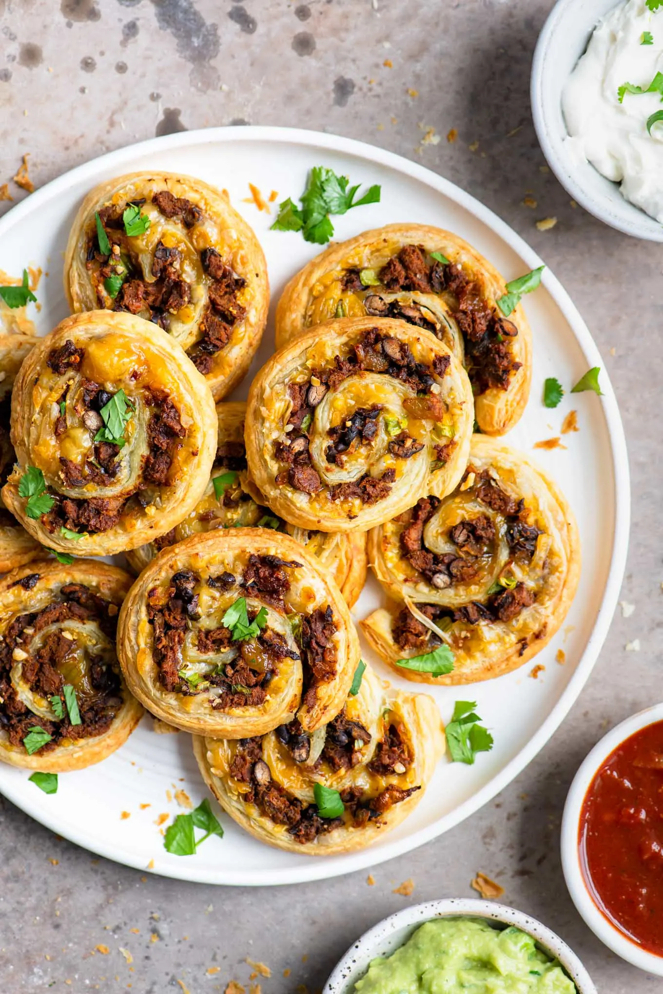 vegan taco pinwheels served with salsa, guacamole, and vegan sour cream